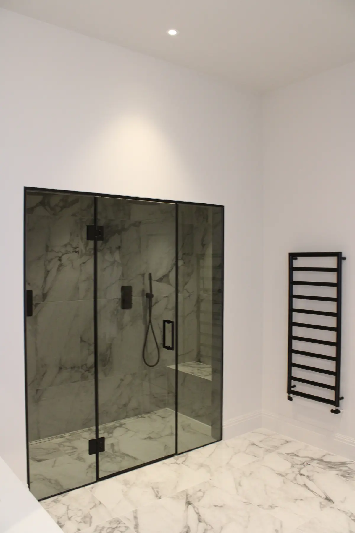 Walk-in shower enclosure with black frame, marble tiles and heated towel rail