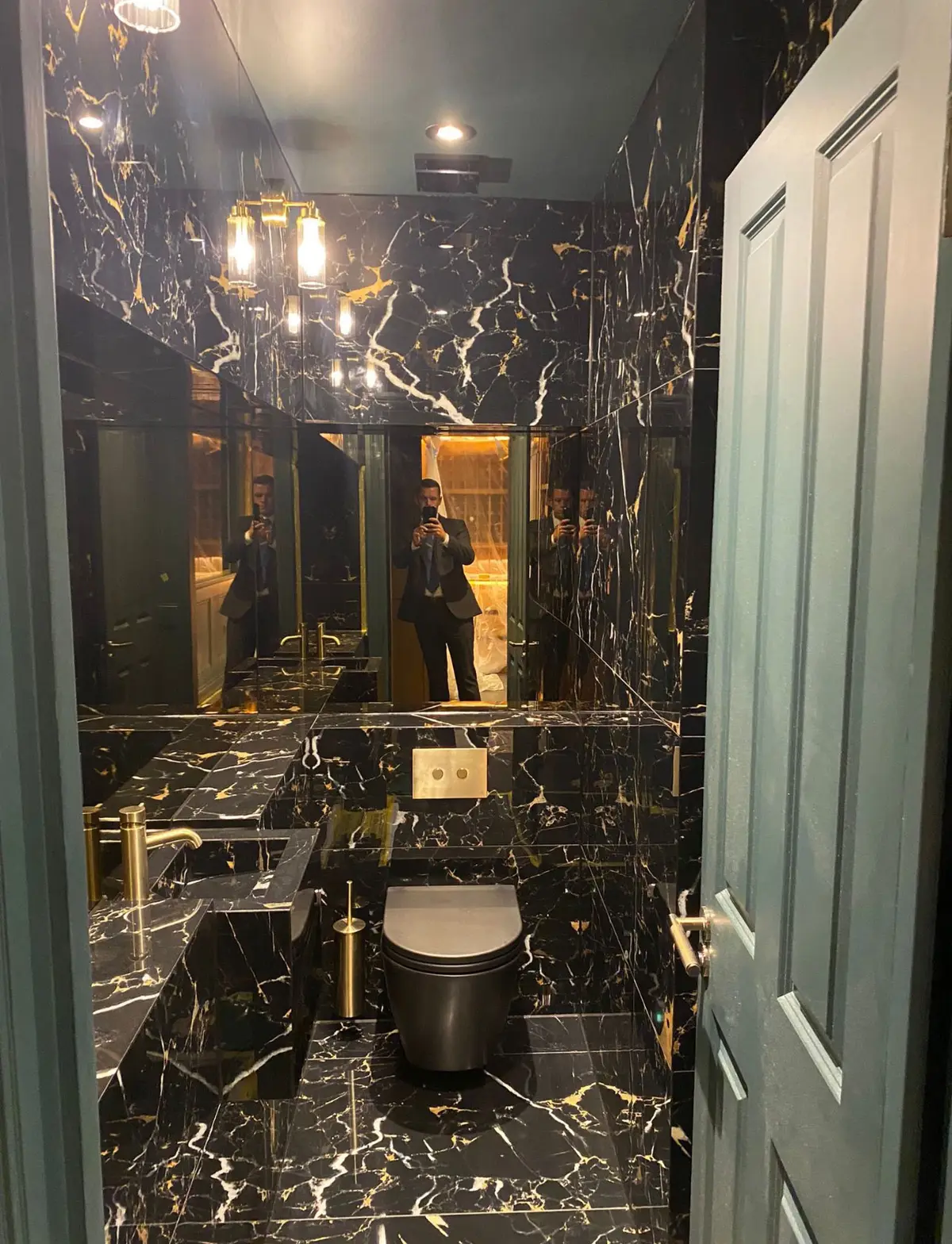 Cloakroom with dark veined marble walls, brass tap and wall-hung toilet
