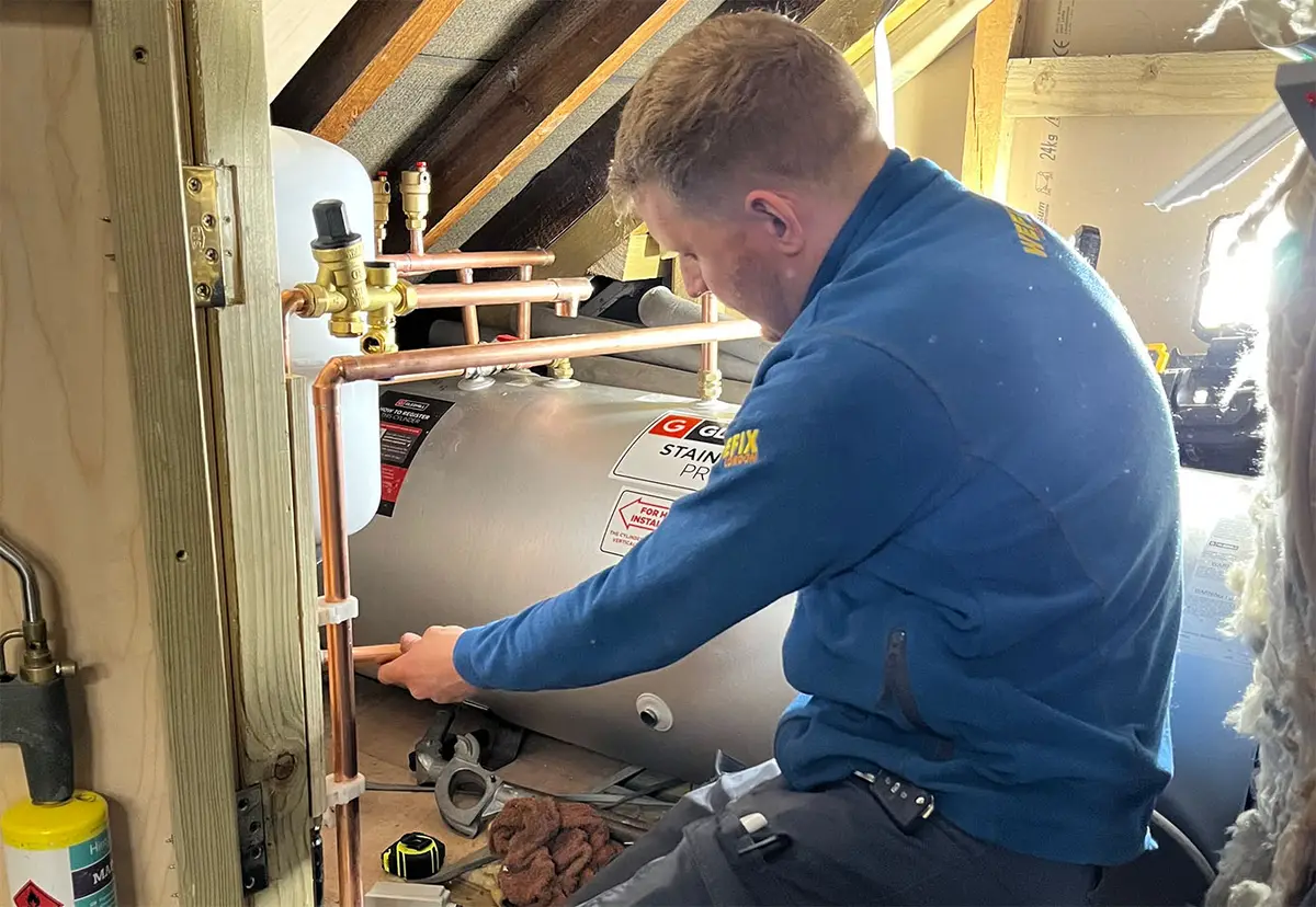 Heating engineer working on a hot water cylinder in a loft
