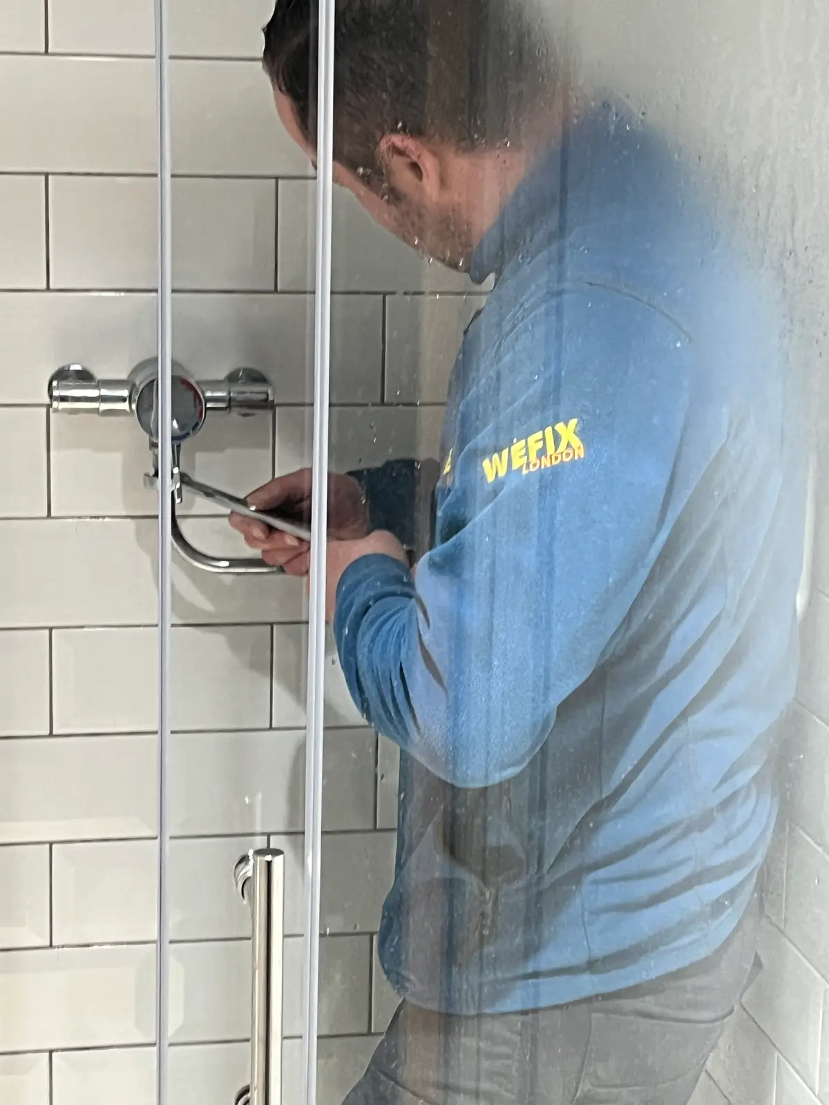 Plumber fitting a thermostatic shower valve on a tiled wall