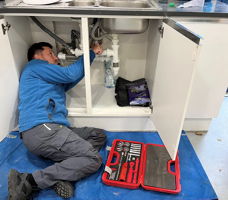 Engineer working under a sink unit with tool kit laid out